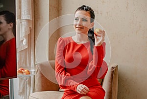 Young girl in a red indoors. Pensive model. Emotions of a modern lady. Girl eating an apple