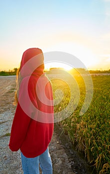 Young girl with red jacket from behind in a rice field at sunset time. Concept tranquility, nature, chromatic contrast