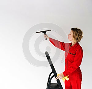 a young girl in a red jumpsuit, an employee of a cleaning company, stands on a stepladder and holds a glass scraper in