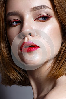 Young girl with red lips and red arrows in front of eyes. Beautiful model with makeup nude and shining skin. Photo taken in the st