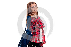 A young girl in a red Plaid Shirt and with a portfolio on the shoulders of stands sideways and smiling