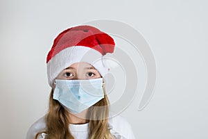 Young girl with red santa claus hat and mask isolated on white background. Sad child face with surgical mask. Christmas covid 19