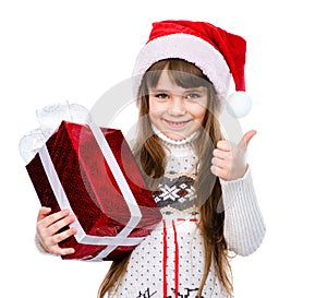 Young girl with red santa hat holding gift box and showing thumbs up. isolated on white background