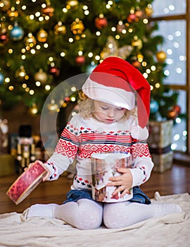 Young girl in red santa hat opening Christmas gifts
