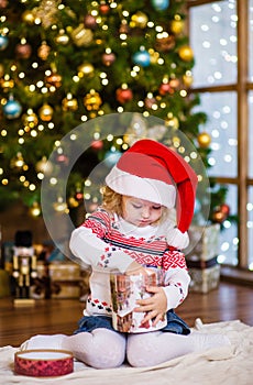 Young girl in red santa hat opening Christmas gifts