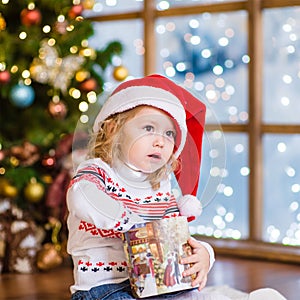 Young girl in red santa hat opening Christmas gifts