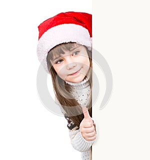Young girl in red santa hat standing behind white board and showing thumbs up. on white