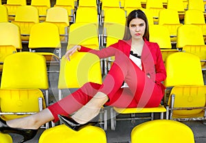 Young girl in a red suit smiles and sits on an empty tribune of the stadium