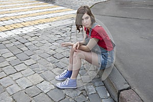 Young girl in a red wool sweater and jeans shorts is sitting on the steps