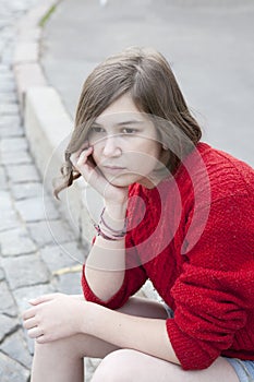 Young girl in a red wool sweater and jeans shorts is sitting on the steps