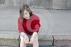 Young girl in a red wool sweater and jeans shorts is sitting on the steps