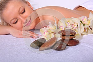 A young girl relaxes in a spa by lying on her stomach next to orchid flowers and heated stones