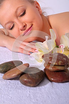 A young girl relaxes in a spa while lying on her stomach next to orchid flowers and heated stones. Close-up view