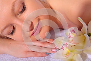 A young girl relaxes in a spa while lying on her stomach next to orchid flowers and heated stones. Close-up view