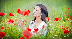 Young girl relaxing in green poppies field. Portrait of beautiful brunette woman posing in a field full of poppies