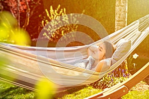 Young girl relaxing having nap in hammock in garden at home at sunset.