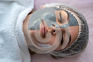 Young girl relaxing at spa, lying in bed with facial mask