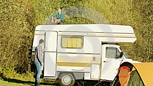 Young girl relaxing on top of retro camper van in mountain wilderness