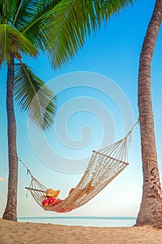 Young girl resting in a hammock under tall palm trees, tropical beach