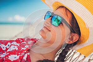 Young girl resting in a hammock under tall palm trees, tropical beach