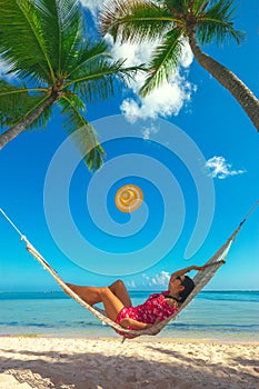 Young girl resting in a hammock under tall palm trees, tropical beach