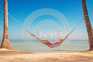 Young girl resting in a hammock under tall palm trees, tropical beach