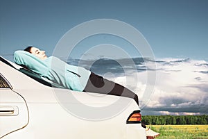 A young girl resting on the trunk of a car against the backdrop of an incipient thunderstorm, during a long journey on a suburban