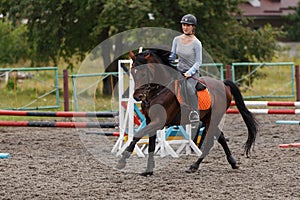 Young girl riding bay horse on show jumping training