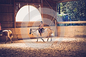 A young girl riding a horse in arena.