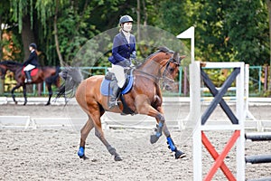 Young girl riding sorrel horse on show jumping