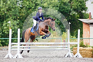 Young girl riding sorrel horse on show jumping