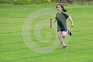 Young girl running relay race on grass running track outdoors