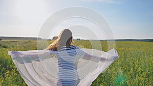 A young girl runs around a rapeseed field with a white cloth. Romantic theme.