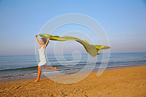 Young girl runs on edge of sea with yellow shawl
