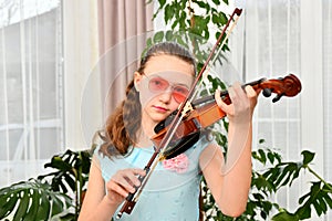 A young girl runs her bow across the strings of a violin and looks into the camera