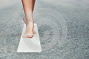 Young girl`s bare feet stand on the divivding road line