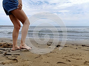 Young girl`s legs on the sand on the beach at the water`s edge