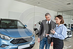 Young girl sales consultant with a clipboard who advises a male client in a car dealership.