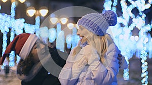 Young girl in santa`s hat makes a suprise with a present for her friend