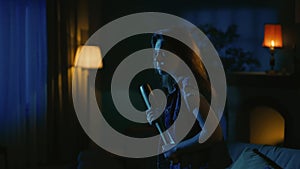 Young girl with scaried face expression walking in the dark living room, looking around, holding baseball bat in hand.