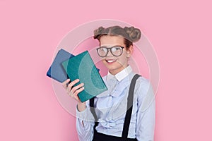 Young girl in school uniform and glasses holding books in her hands on pink background