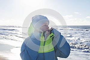 A young girl at the sea on a sunny day in winter. A pretty blonde in a blue hat and a bright sports jacket. Active recreation and