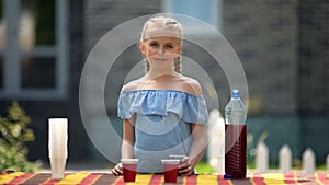 Young girl selling lemonade on yard sale, first money earning, organic beverage