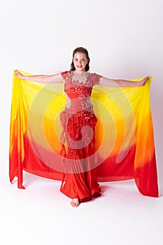 Young girl with shawl and in red dress performs oriental dance on white background