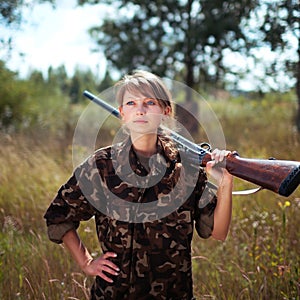 Young girl with a shotgun looks into the distance in an outdoor