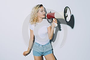 Young blonde girl shouting by megaphone isolated on white background