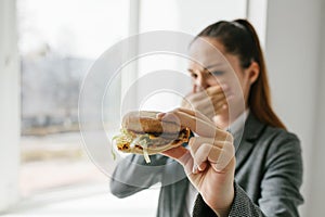 A young girl shows that she does not like a burger. Conceptual image of refusal from unhealthy eating.