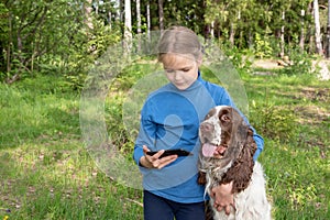 A young girl shows something to her dog in a mobile phone. A child plays with a dog and telephone