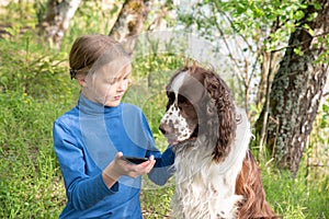 A young girl shows something to her dog in a mobile phone. A child plays with a dog and telephone