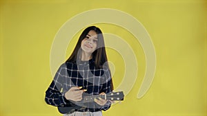 Young girl singing and playing ukulele on yellow Background in Studio